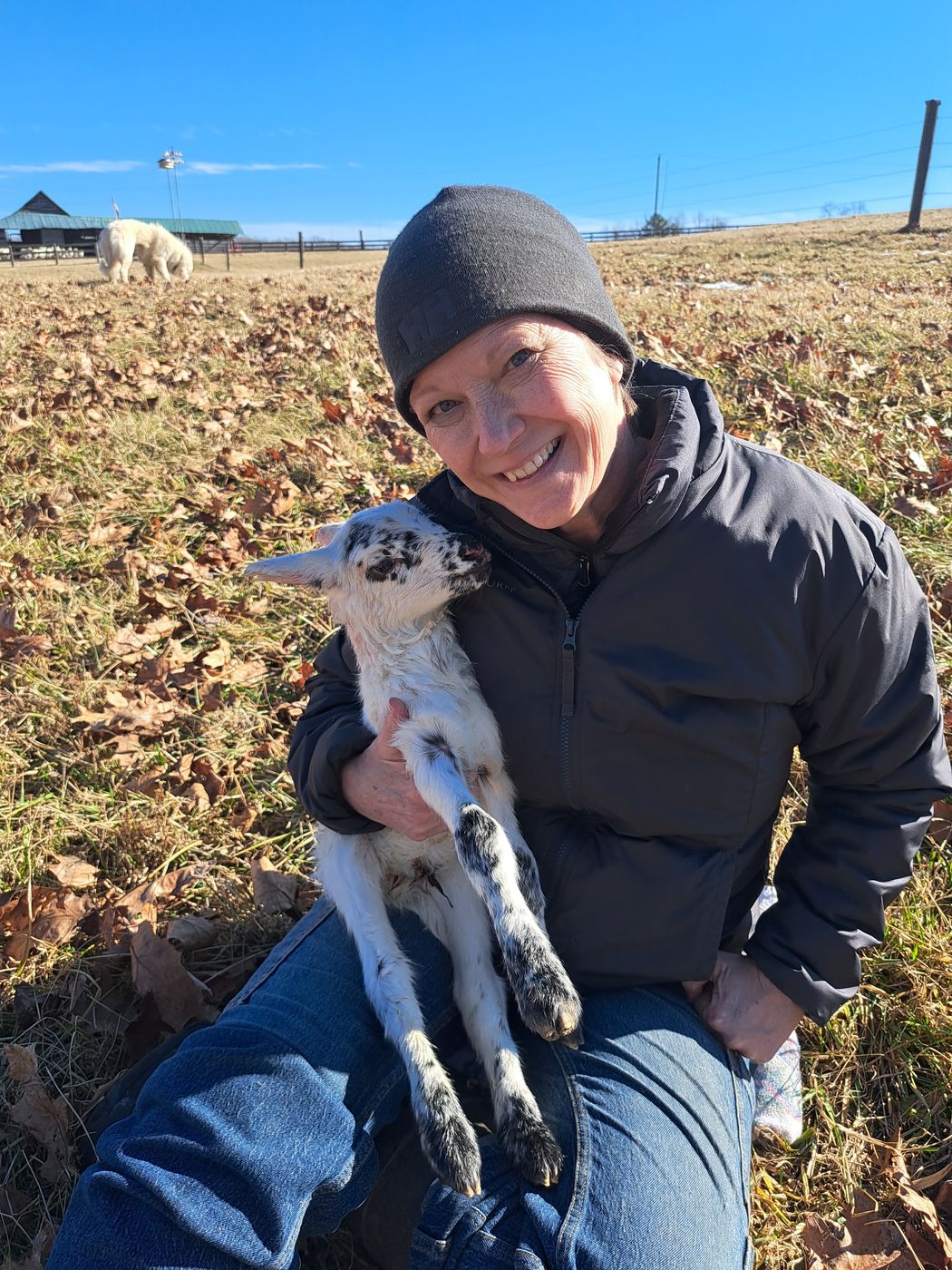 Steph holding a spotted newborn lamb in the pasture